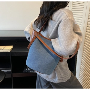Detail view of denim bucket bag with brown leather trim and metal rivets on model