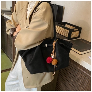 Détail du sac cabas noir avec boucle en métal et accessoire pompon en peluche bicolore