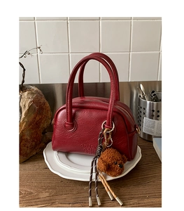 Detail of burgundy bowling bag with lychee texture and enjoy engraving and bear charm
