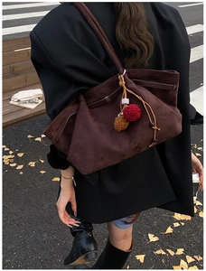 Détail d'un grand sac cabas en daim marron avec breloques en peluche dans un décor d'automne