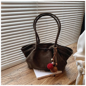 Détail du sac cabas en daim vert olive avec breloque pompon colorée posé sur un livre