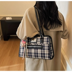 Detail of vintage plaid tote bag with plush charm and black leather trim on model