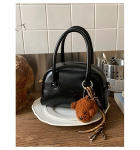 Detail of a black bowling bag with vintage texture and cute plush bear tassel charm