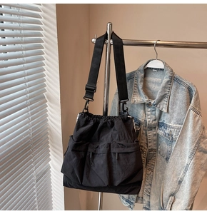 Detail of black nylon shoulder bag showing drawstring closure and double front flap pockets