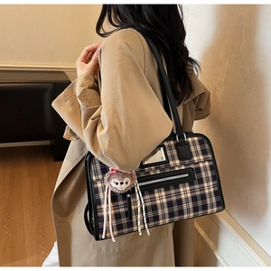 Detailed view of vintage plaid tote bag with black leather straps on a khaki trench coat