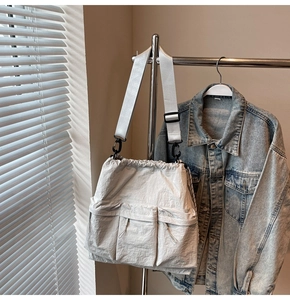 Close-up of light grey nylon shoulder bag with triple front pockets and drawstring