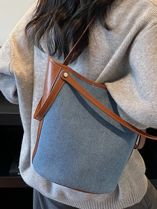 Chic blue denim bucket bag with brown leather trim worn by model in a cozy setting