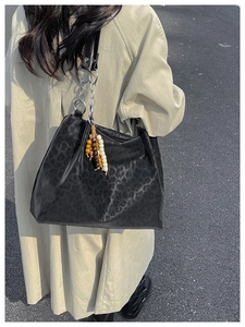 Detail of black leopard print tote bag with metal chain strap and wooden bead tassel