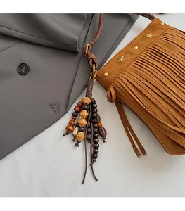 Gros plan sur un sac bandoulière en daim marron avec rivets et pompon ethnique