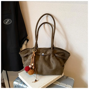 Détail d'un sac cabas en daim avec breloques posé sur une valise et un livre d'art