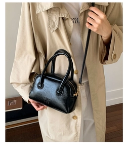 Detail of glossy black leather bowling bag with gold hardware and dual handles