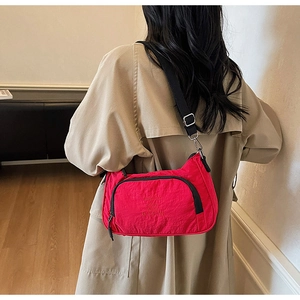 Detail view of a vibrant red nylon half-moon crossbody bag with black zipper and text design