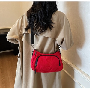 Detail of red nylon crossbody bag with black strap and zipper on a beige trench coat