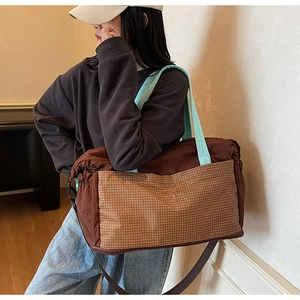 Detail showing checkered front pocket and blue webbing handle on brown tote bag