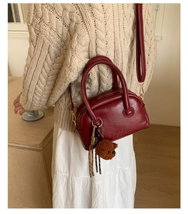 Detail of burgundy glossy leather bowling bag featuring side embossing and plush bear charm