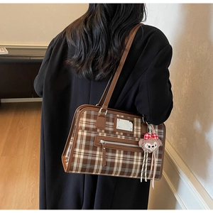 Detail of vintage brown plaid tote bag with plush charm and side zipper on black coat