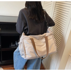 Detail of a beige tote bag with brown straps showing grid texture and side drawstring pocket