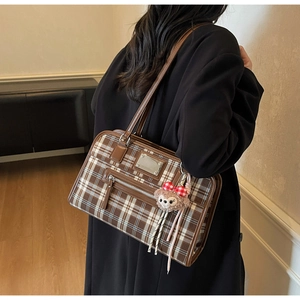 Detail view of plaid tote bag with dark brown leather handles and plush charm accessory