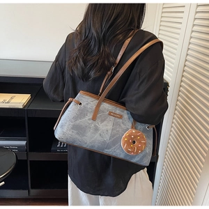 Dettaglio della borsa tote in denim blu lavato con manici in pelle marrone e ciondolo