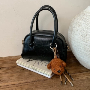 Detail of black glossy wrinkled bowling bag with cute plush puppy charm on wood surface