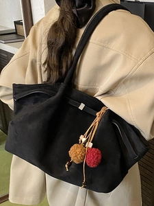 Grand sac cabas noir en daim avec pompon décoratif porté par un mannequin en trench