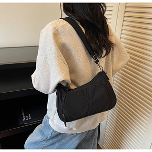 Model wearing black nylon crossbody bag with wide shoulder strap and embroidery detail