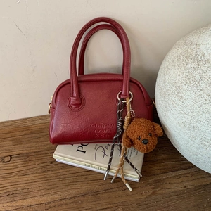Close-up of vintage red lychee leather bowling bag with teddy bear charm on books