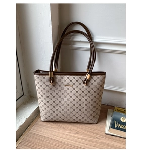 Detail of khaki tote bag with geometric patterns, gold hardware, and dark brown straps