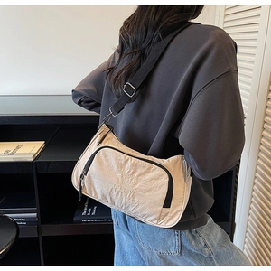 Detail of light beige pleated nylon crossbody bag with black zipper and text embroidery