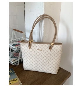 Detail view of cream tote bag with geometric pattern and khaki leather handles on wooden table