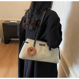 Dettaglio borsa tote in pelle scamosciata grigio-verde con spalline nere e ciondolo donut