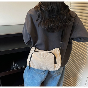 Detail of cream nylon crossbody bag with black zipper and embroidered text on the side
