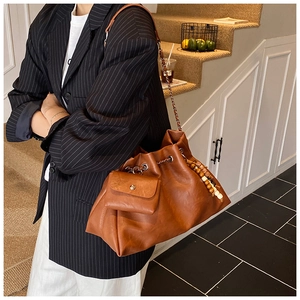 Detail of retro brown leather bucket bag with chain strap and ethnic beaded charm decoration