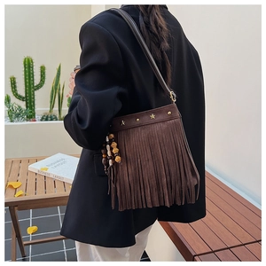 Détail du sac bandoulière en daim marron avec rivets en étoile et pompon à perles