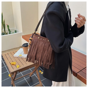 Détail d'un sac à bandoulière marron avec franges, rivets étoiles et perles de bois boho