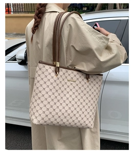 Detail of a large monogram tote bag worn on shoulder by a model in a light trench coat