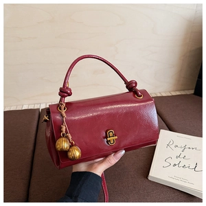Detail of burgundy leather handbag featuring golden ball charms and decorative knots