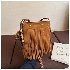 Détail d'un sac bandoulière en daim marron avec pompons, étoiles dorées et perles