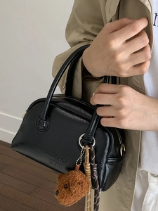 Stylish retro black leather bowling handbag featuring a cute teddy bear charm accessory