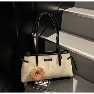 Dettaglio borsa beige con cinturini in pelle nera e ciondolo a ciambella di peluche
