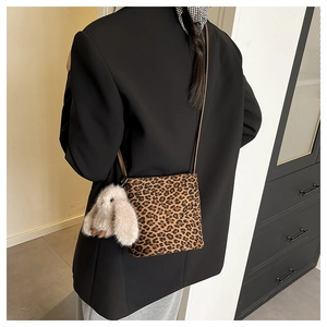 Detail of leopard print crossbody bag with fluffy white bunny charm and brown leather strap