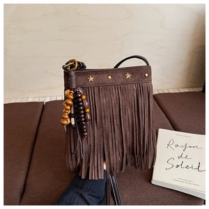 Détail de sac à bandoulière en daim marron avec clous étoilés et pompons en perles de bois