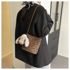 Detail of leopard print crossbody bag featuring a white plush bunny charm on brown strap