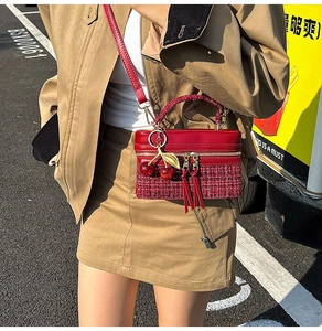 Detail of red tweed and leather crossbody bag featuring decorative cherry charms and strap