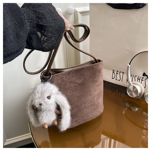 Detail of dark brown frosted suede bucket bag featuring a cute grey plush rabbit pendant