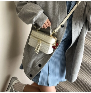 Detail view of cream tweed box bag with cherry charm and chain on a stylish model