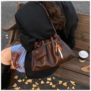 Deep brown bucket shoulder bag with chain strap and beaded pendant in outdoor setting