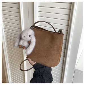Detail of a brown matte suede bucket bag with a cute plush rabbit pendant and slim strap