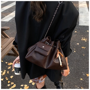 Detail of dark brown leather bucket bag with wooden bead charm and woven chain strap