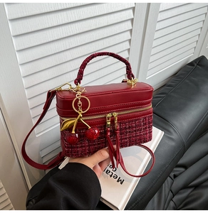 Detail of red tweed and leather box bag with cherry charm and gold zipper accents